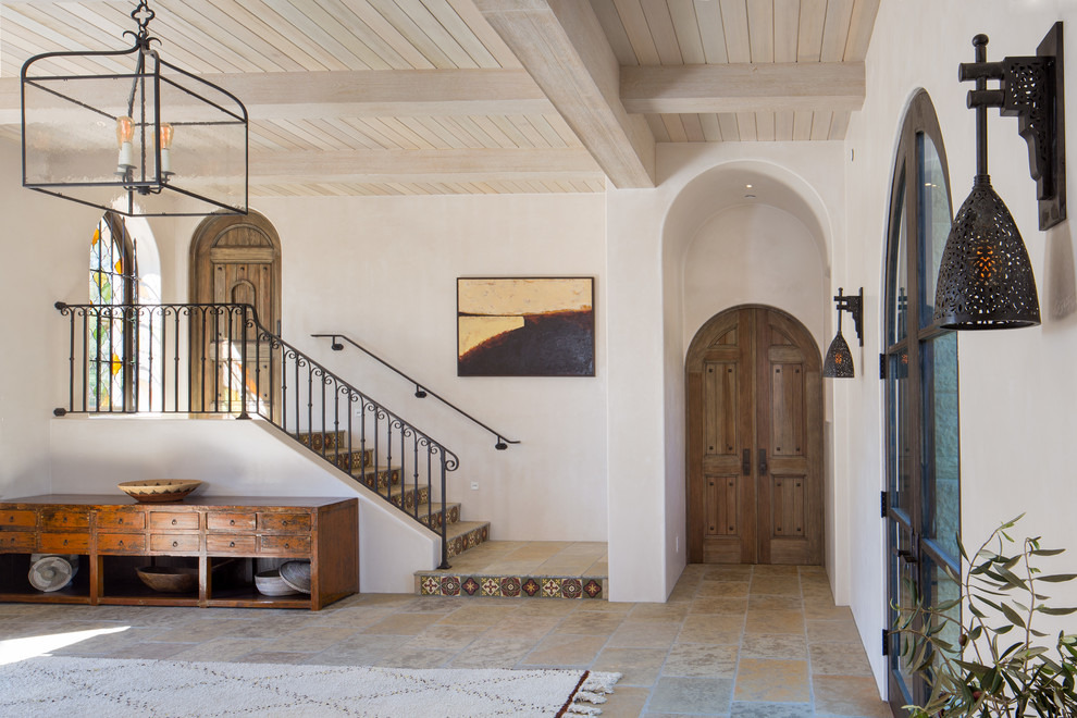 This is an example of a large mediterranean foyer in Santa Barbara with white walls, limestone floors, a double front door, a dark wood front door and beige floor.