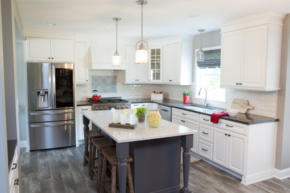 Mid-sized transitional l-shaped eat-in kitchen in Chicago with a farmhouse sink, recessed-panel cabinets, white cabinets, quartzite benchtops, white splashback, travertine splashback, stainless steel appliances, vinyl floors, with island, grey floor and grey benchtop.