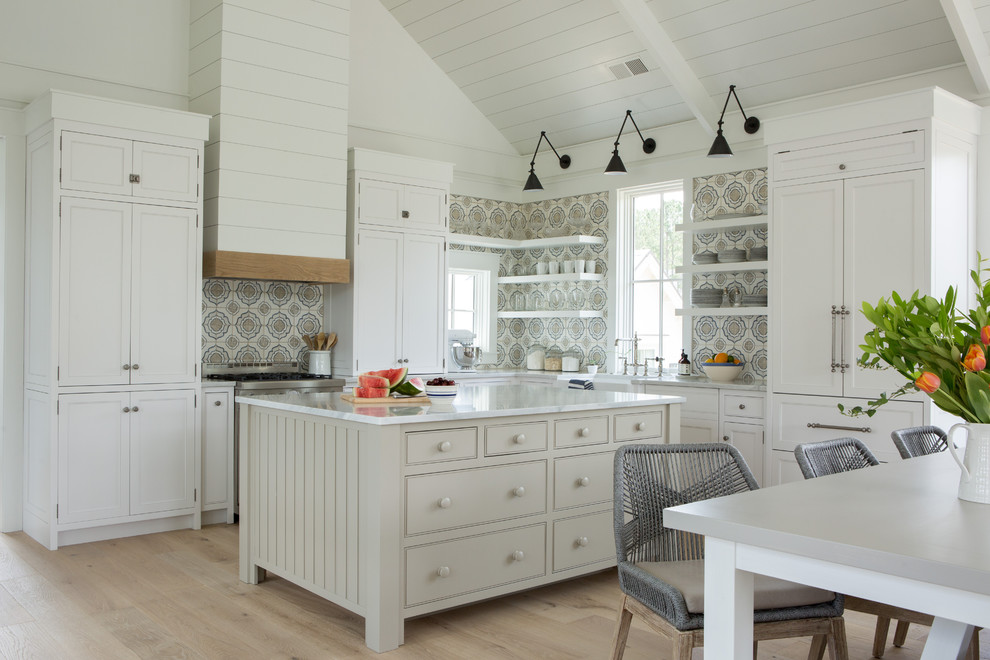 Inspiration for a mid-sized beach style l-shaped eat-in kitchen in Philadelphia with a farmhouse sink, shaker cabinets, white cabinets, multi-coloured splashback, panelled appliances, light hardwood floors, with island, beige floor, white benchtop, marble benchtops and terra-cotta splashback.