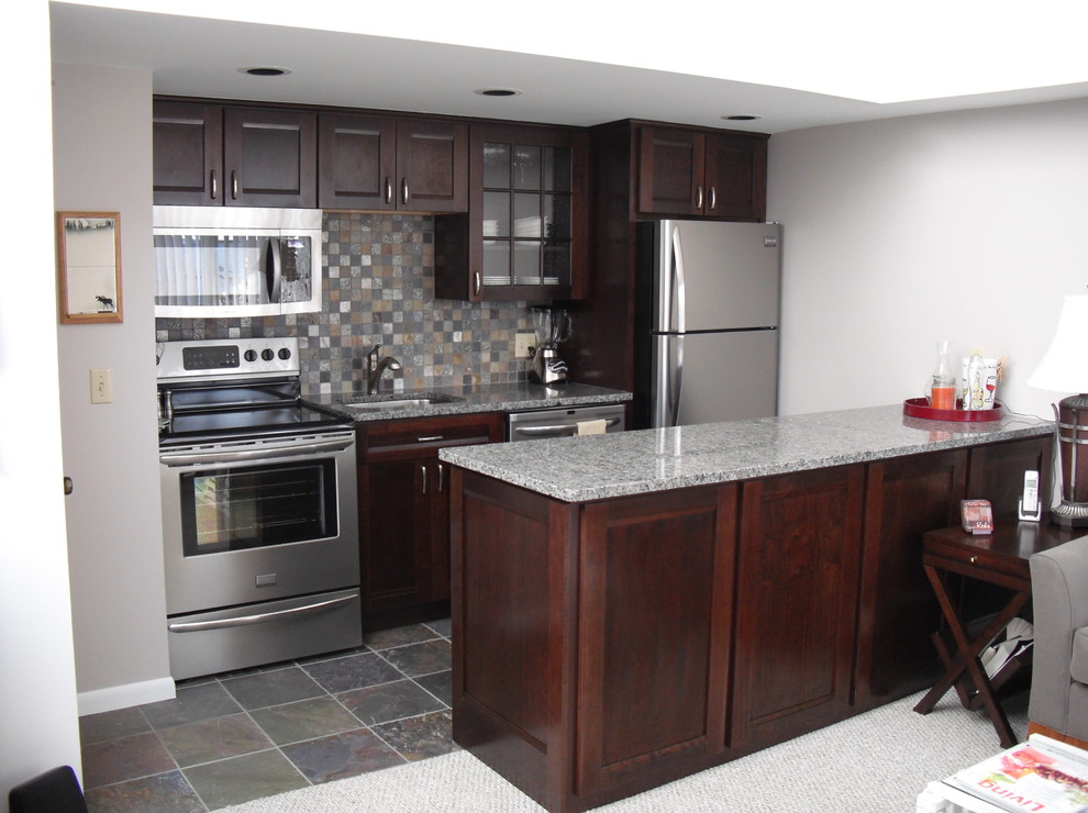Kitchen - small galley porcelain tile kitchen idea with a single-bowl sink, flat-panel cabinets, dark wood cabinets, granite countertops, gray backsplash, mosaic tile backsplash, stainless steel appliances and a peninsula