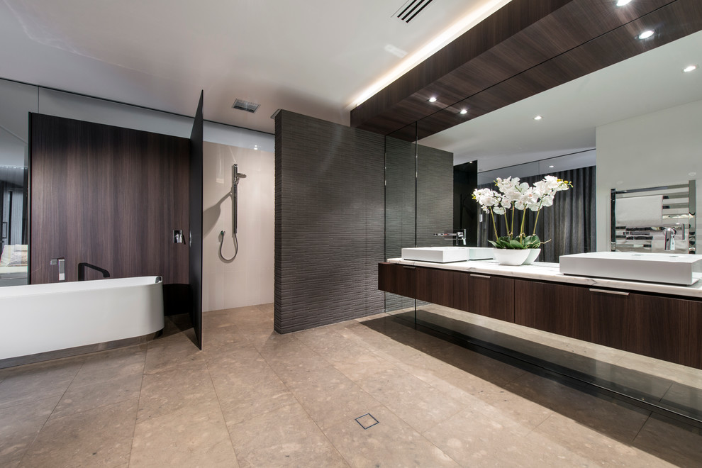 This is an example of an expansive contemporary master bathroom in Perth with a vessel sink, flat-panel cabinets, dark wood cabinets, marble benchtops, a freestanding tub, an open shower, a wall-mount toilet, white tile, ceramic tile, white walls and limestone floors.