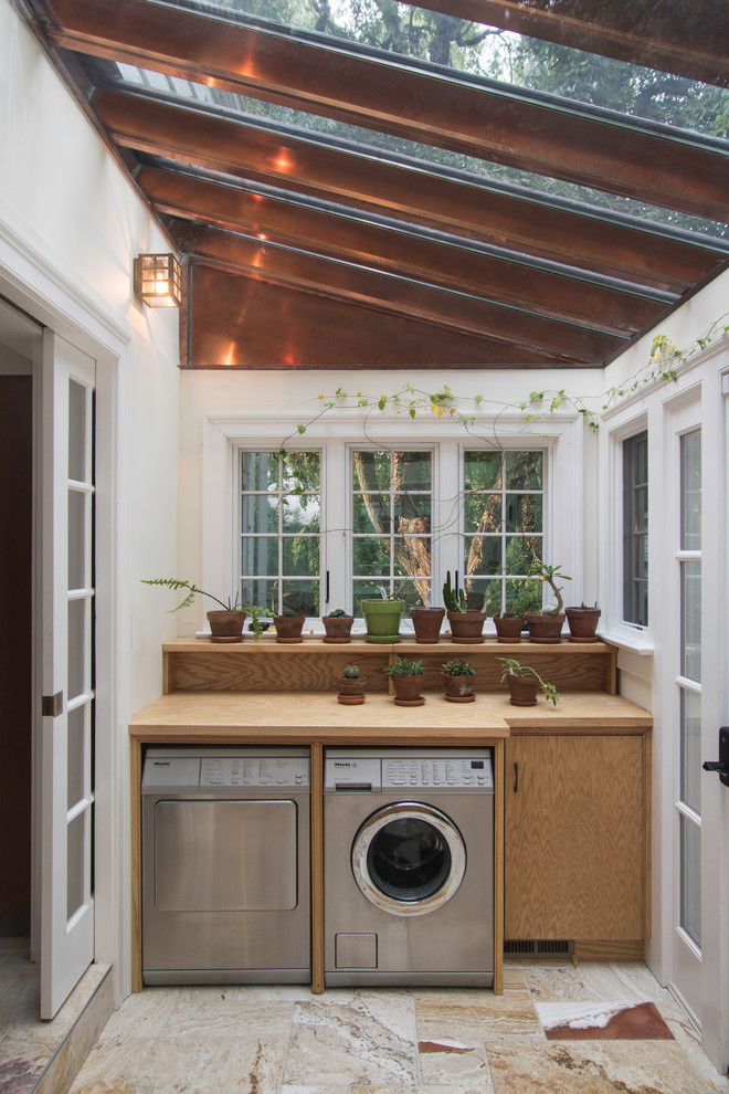 Small traditional single-wall utility room in New York with flat-panel cabinets, light wood cabinets, wood benchtops, white walls, travertine floors and a side-by-side washer and dryer.