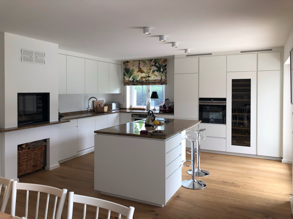 Immagine di una cucina minimal di medie dimensioni con lavello integrato, ante lisce, top in pietra calcarea, paraspruzzi bianco, elettrodomestici neri, parquet chiaro, pavimento beige e top beige