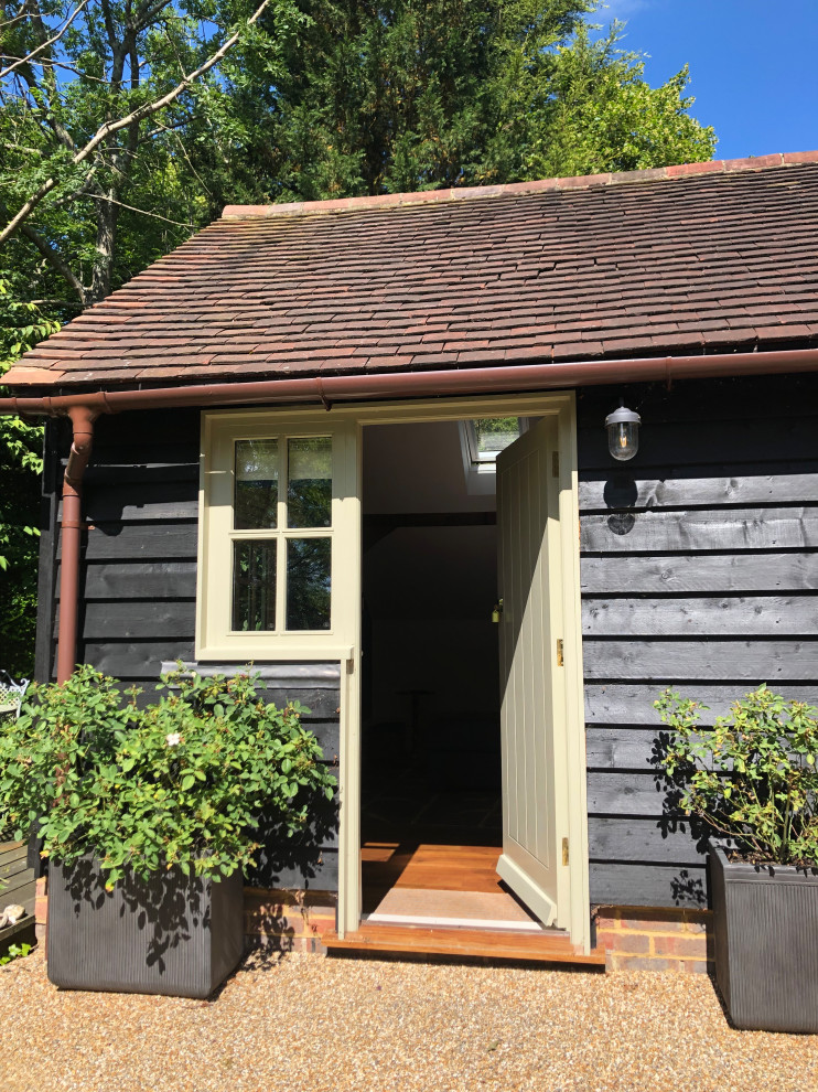 This is an example of a small industrial one-storey black house exterior in Sussex with wood siding, a butterfly roof, a tile roof, a red roof and board and batten siding.