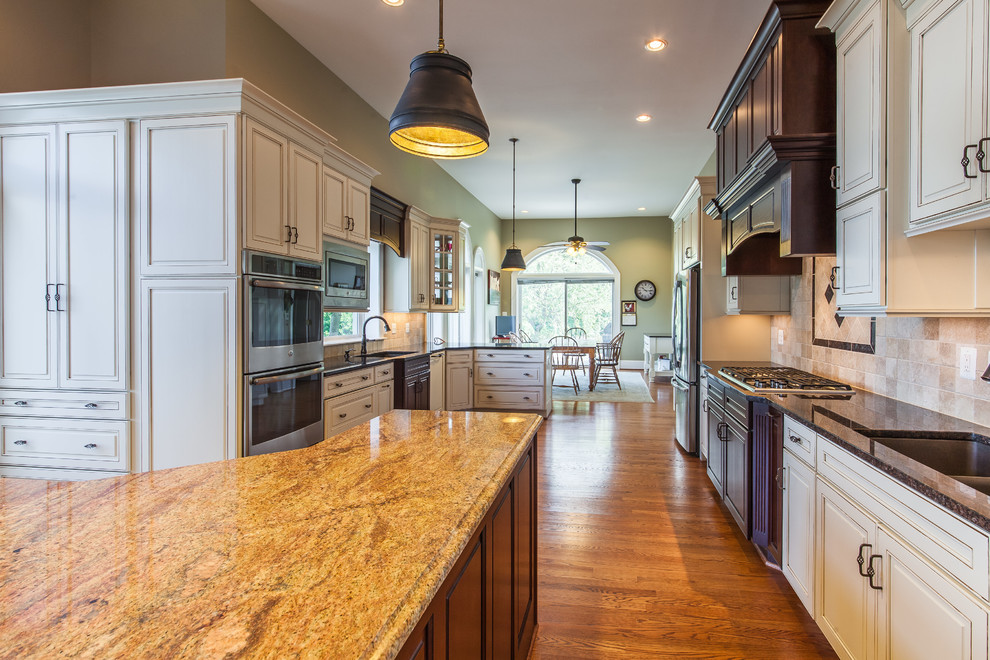 Eat-in kitchen - huge transitional medium tone wood floor eat-in kitchen idea in DC Metro with raised-panel cabinets, granite countertops, stainless steel appliances and an island