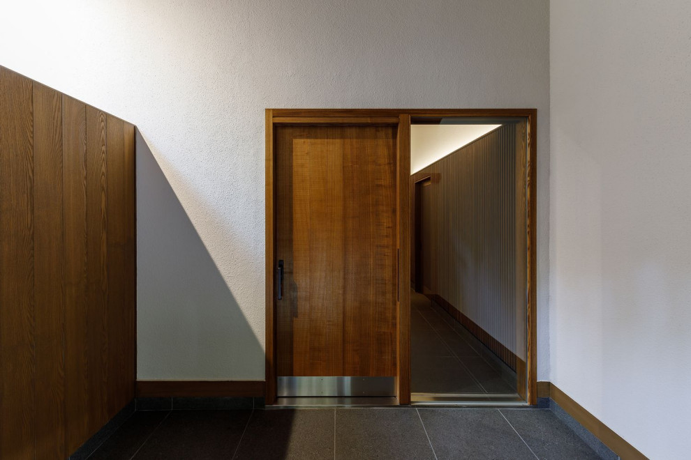 Diseño de hall asiático grande con paredes blancas, suelo de baldosas de cerámica, puerta corredera, puerta marrón, suelo gris y madera