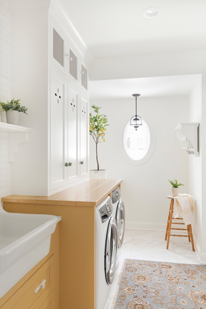 Photo of a mid-sized country single-wall utility room in Minneapolis with a drop-in sink, beaded inset cabinets, yellow cabinets, a side-by-side washer and dryer, white floor and yellow benchtop.