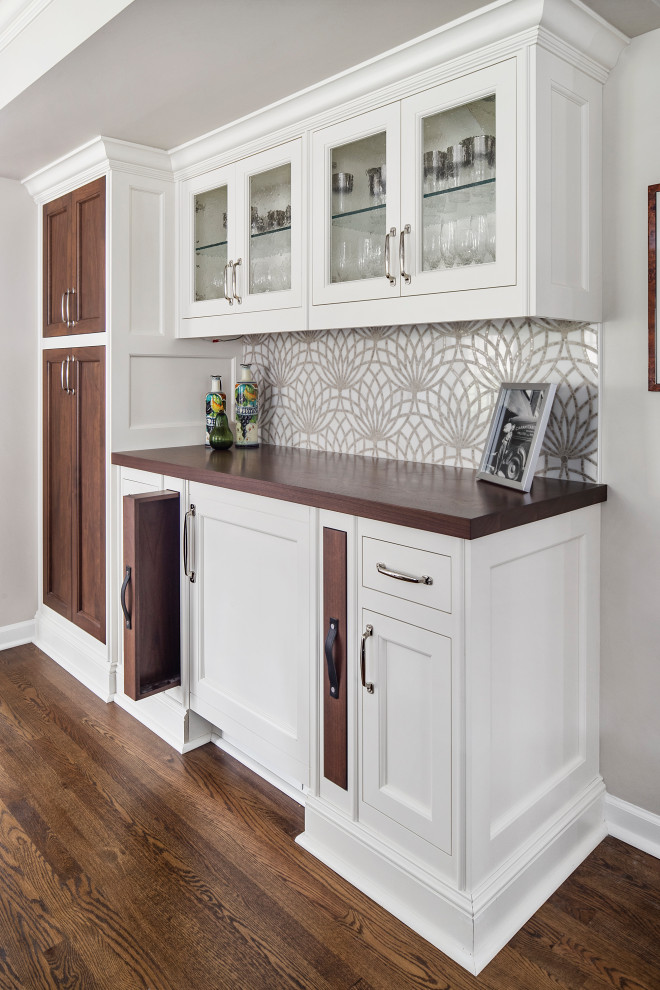 Photo of a large transitional single-wall home bar in Detroit with white cabinets, dark hardwood floors, brown floor, no sink, glass-front cabinets, wood benchtops, multi-coloured splashback and brown benchtop.
