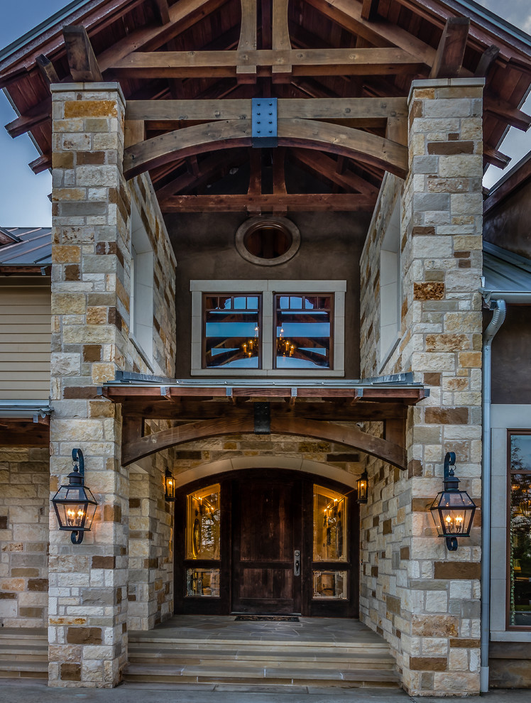 Photo of a large country one-storey beige house exterior in Houston with stone veneer, a gable roof and a metal roof.