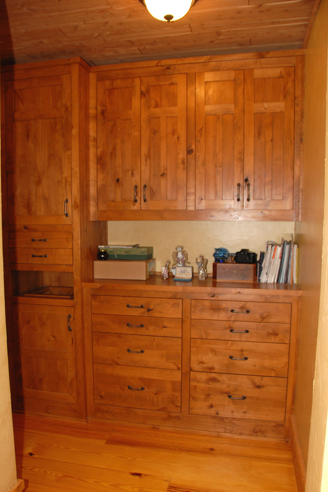 Photo of a mid-sized country single-wall laundry cupboard in Portland with medium wood cabinets, wood benchtops, beige walls, medium hardwood floors, a stacked washer and dryer, brown floor and brown benchtop.