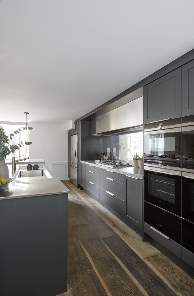 Large contemporary galley open plan kitchen in London with an integrated sink, recessed-panel cabinets, grey cabinets, marble benchtops, metallic splashback, mirror splashback, stainless steel appliances, dark hardwood floors, a peninsula, brown floor and white benchtop.
