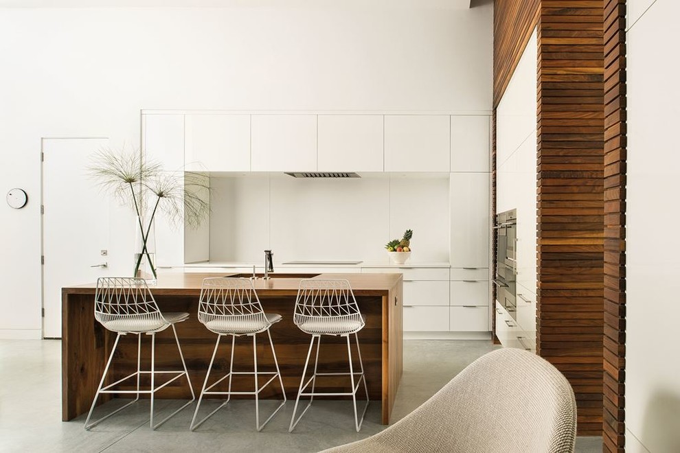 Mid-sized transitional l-shaped concrete floor and gray floor open concept kitchen photo in Austin with an undermount sink, flat-panel cabinets, white cabinets, wood countertops, stainless steel appliances, an island and white backsplash