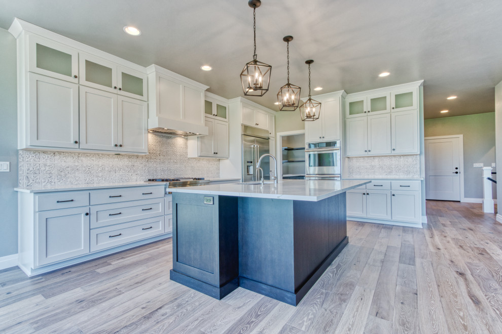 Eat-in kitchen - large transitional l-shaped light wood floor and brown floor eat-in kitchen idea with an undermount sink, shaker cabinets, white cabinets, quartz countertops, white backsplash, ceramic backsplash, stainless steel appliances, an island and white countertops