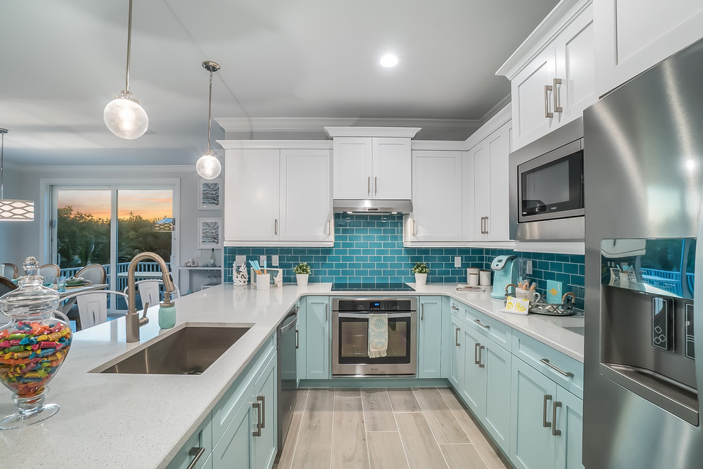 Inspiration for a beach style u-shaped eat-in kitchen in Tampa with an undermount sink, shaker cabinets, blue cabinets, blue splashback, subway tile splashback, stainless steel appliances, a peninsula, beige floor and white benchtop.