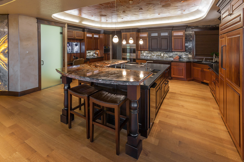 This is an example of an expansive country u-shaped eat-in kitchen in Denver with dark wood cabinets, with island, an undermount sink, raised-panel cabinets, granite benchtops, grey splashback, stone tile splashback, panelled appliances, medium hardwood floors and brown floor.