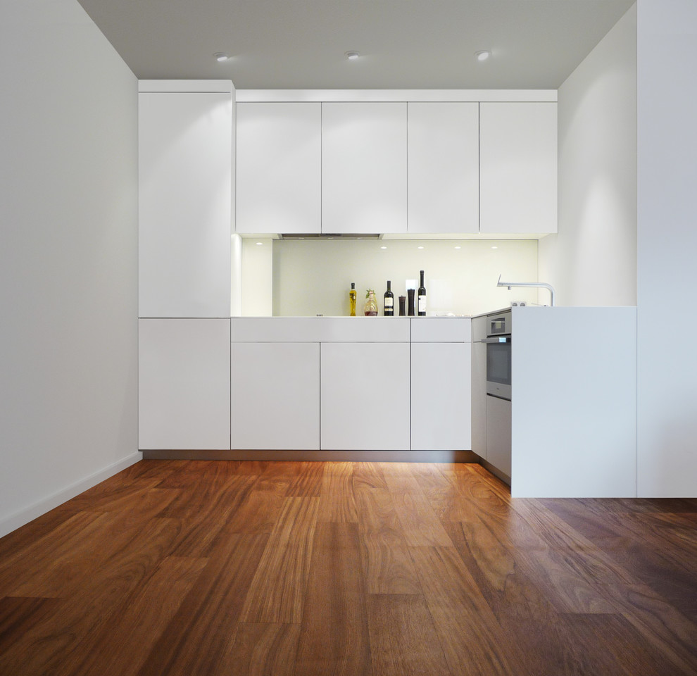 Design ideas for a small contemporary l-shaped open plan kitchen in Berlin with flat-panel cabinets, white cabinets, white splashback, glass sheet splashback, panelled appliances, dark hardwood floors and no island.