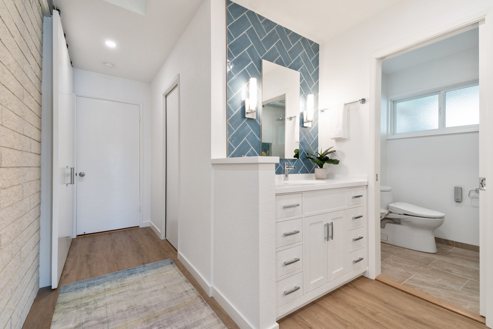 Design ideas for a large beach style master bathroom in San Francisco with shaker cabinets, white cabinets, a bidet, blue tile, ceramic tile, white walls, light hardwood floors, an integrated sink, solid surface benchtops, brown floor, white benchtops, a double vanity and a built-in vanity.