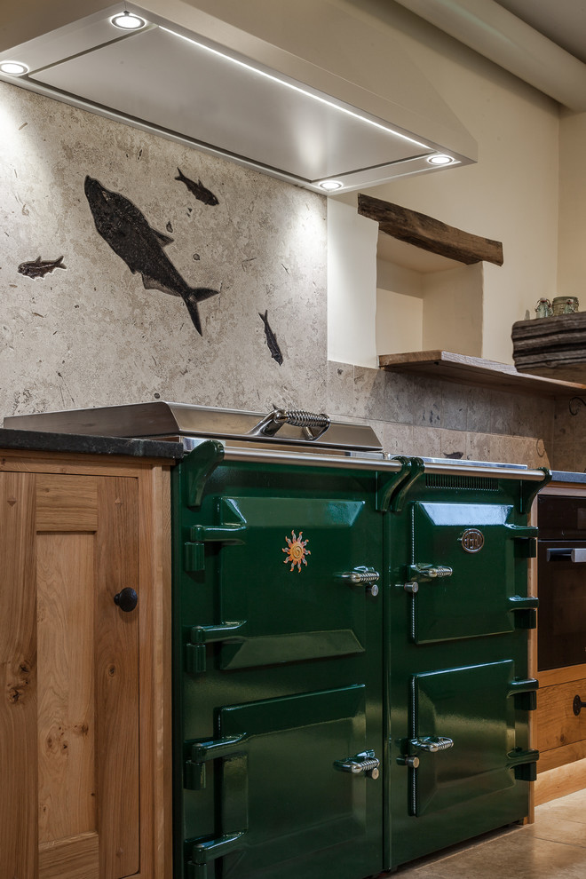 This is an example of a large eclectic u-shaped kitchen in Other with a drop-in sink, raised-panel cabinets, medium wood cabinets, soapstone benchtops, stone slab splashback, coloured appliances, limestone floors and with island.