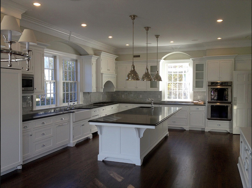 Inspiration for a large transitional l-shaped dark wood floor eat-in kitchen remodel with a farmhouse sink, recessed-panel cabinets, white cabinets, granite countertops, gray backsplash, stone tile backsplash, stainless steel appliances and an island