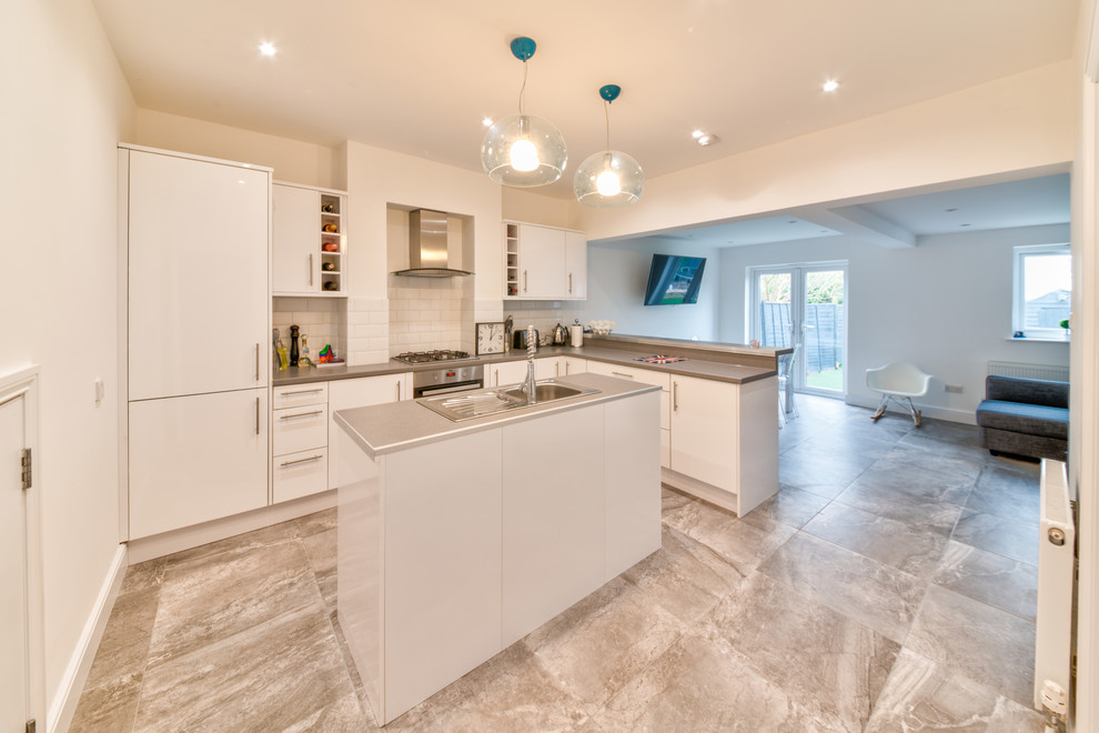 Photo of a mid-sized contemporary l-shaped eat-in kitchen in London with a drop-in sink, flat-panel cabinets, white cabinets, laminate benchtops, white splashback, brick splashback, stainless steel appliances, cement tiles, with island, multi-coloured floor and grey benchtop.