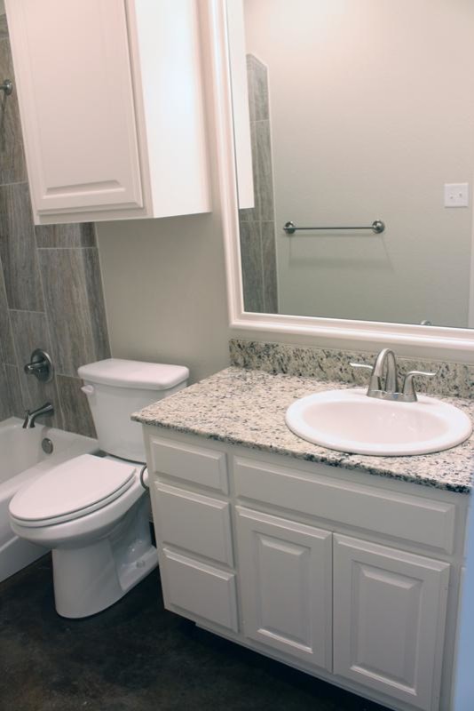 Example of a mid-sized transitional gray tile and porcelain tile concrete floor alcove bathtub design in Austin with raised-panel cabinets, white cabinets, a two-piece toilet, white walls, a drop-in sink and granite countertops