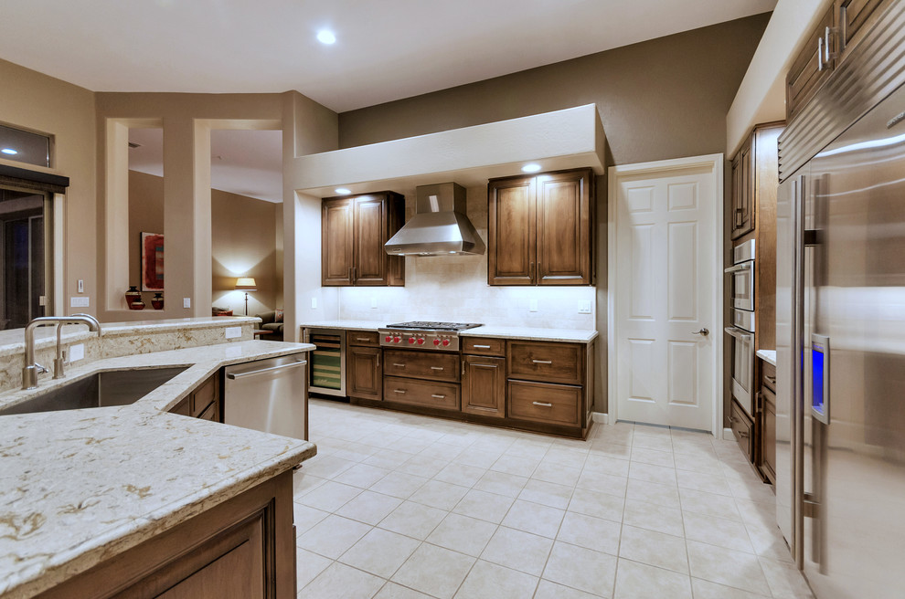 Example of a large transitional l-shaped ceramic tile and white floor open concept kitchen design in Phoenix with an undermount sink, raised-panel cabinets, medium tone wood cabinets, solid surface countertops, white backsplash, stainless steel appliances and an island