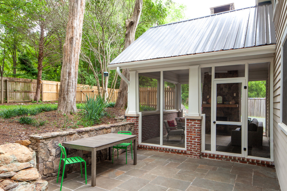 This is an example of a small traditional backyard screened-in verandah in Raleigh with natural stone pavers and a roof extension.