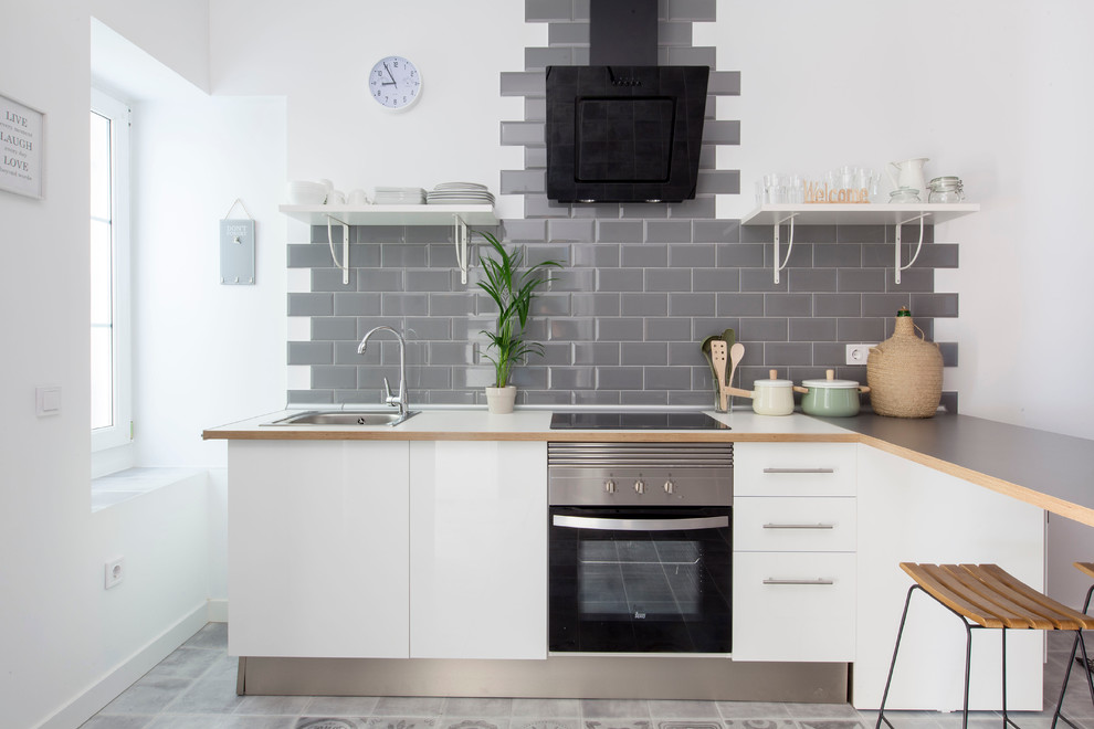 Photo of a mid-sized scandinavian l-shaped open plan kitchen in Madrid with flat-panel cabinets, white cabinets, wood benchtops, grey splashback, subway tile splashback, stainless steel appliances, a drop-in sink and a peninsula.