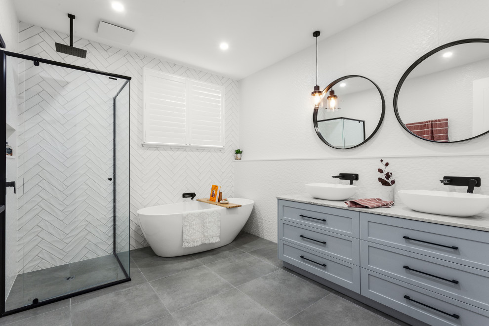 Photo of a medium sized contemporary family bathroom in Melbourne with shaker cabinets, grey cabinets, a freestanding bath, a double shower, a wall mounted toilet, white tiles, marble tiles, white walls, ceramic flooring, marble worktops, grey floors, a hinged door, a wall niche, double sinks and a freestanding vanity unit.