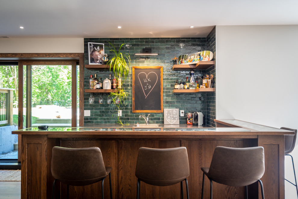 Design ideas for a small traditional l-shaped wet bar in Other with a built-in sink, shaker cabinets, brown cabinets, glass worktops, green splashback, ceramic splashback and white worktops.