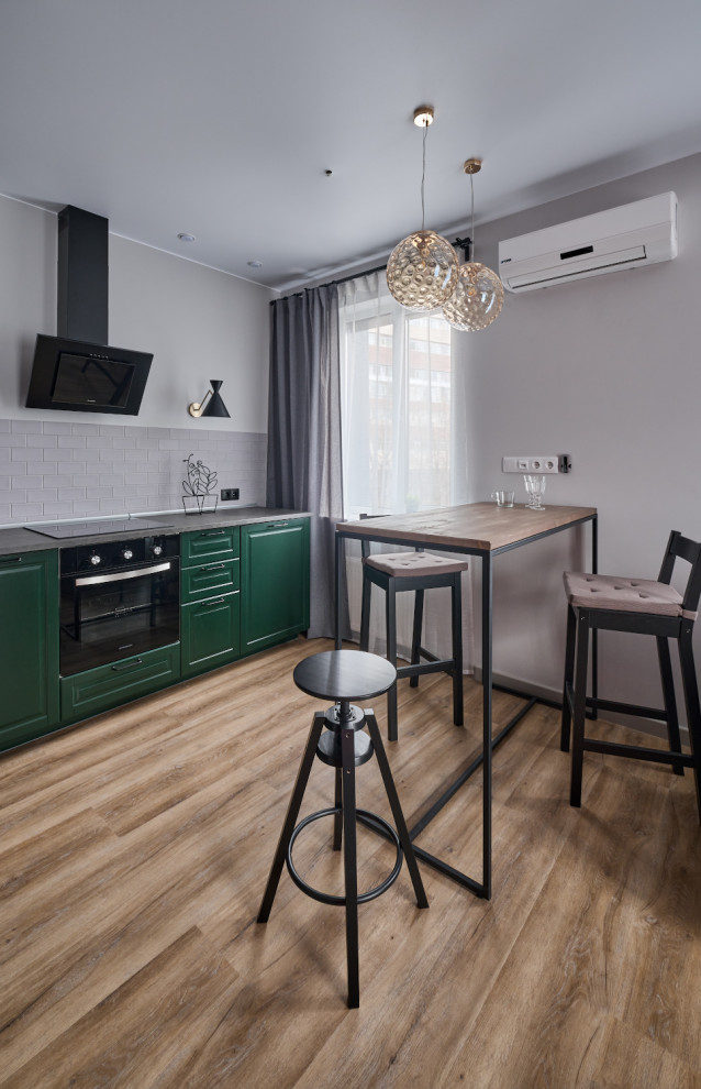 Foto på ett mellanstort funkis grå kök, med en nedsänkt diskho, luckor med infälld panel, gröna skåp, laminatbänkskiva, grått stänkskydd, stänkskydd i keramik, svarta vitvaror, vinylgolv och brunt golv