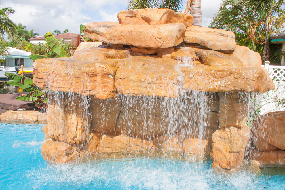 This is an example of a large tropical backyard custom-shaped pool in Miami with a water slide and natural stone pavers.