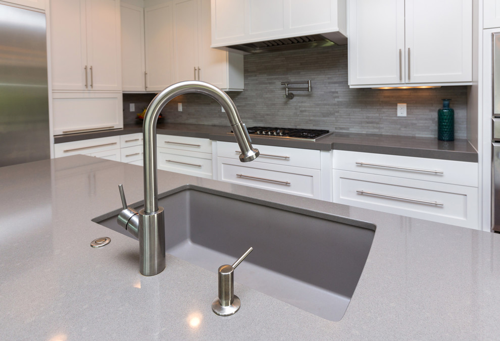 Large transitional l-shaped dark wood floor eat-in kitchen photo with an undermount sink, shaker cabinets, white cabinets, solid surface countertops, gray backsplash, stainless steel appliances and an island