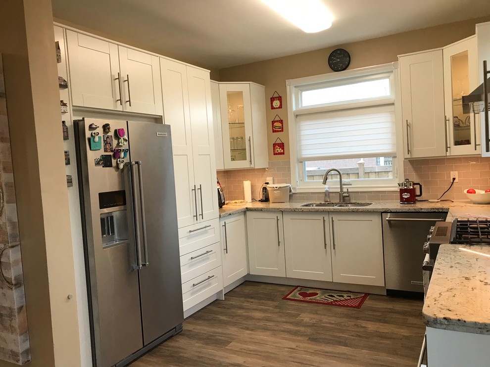 This is an example of a large u-shaped open plan kitchen in Toronto with a double-bowl sink, shaker cabinets, white cabinets, granite benchtops, grey splashback, subway tile splashback, stainless steel appliances, laminate floors, no island, brown floor and grey benchtop.