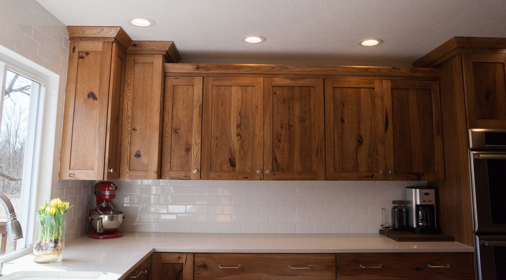 Inspiration for a mid-sized rustic l-shaped light wood floor kitchen remodel in Indianapolis with a single-bowl sink, flat-panel cabinets, medium tone wood cabinets, quartz countertops, white backsplash, subway tile backsplash, stainless steel appliances, white walls, an island and white countertops