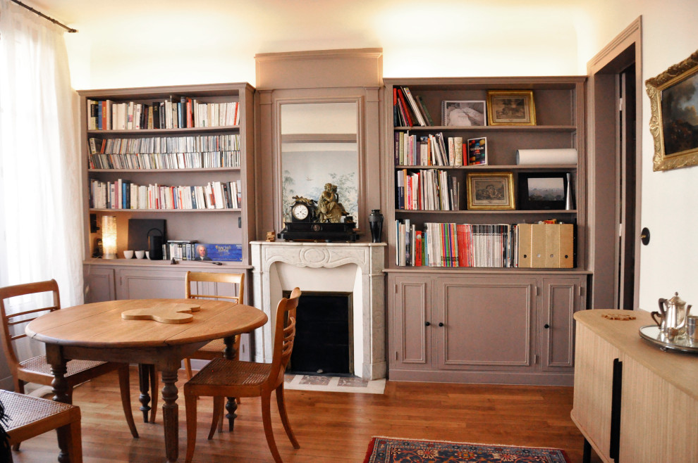 На фото: открытая гостиная комната среднего размера в стиле неоклассика (современная классика) с с книжными шкафами и полками, бежевыми стенами, светлым паркетным полом, стандартным камином и отдельно стоящим телевизором