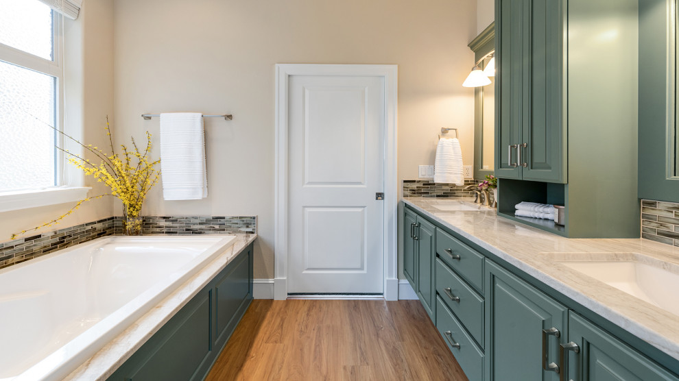 Photo of a mid-sized traditional master bathroom in Other with raised-panel cabinets, green cabinets, a drop-in tub, beige tile, beige walls, an undermount sink, quartzite benchtops, brown floor, a hinged shower door, beige benchtops, an enclosed toilet, a double vanity and a built-in vanity.