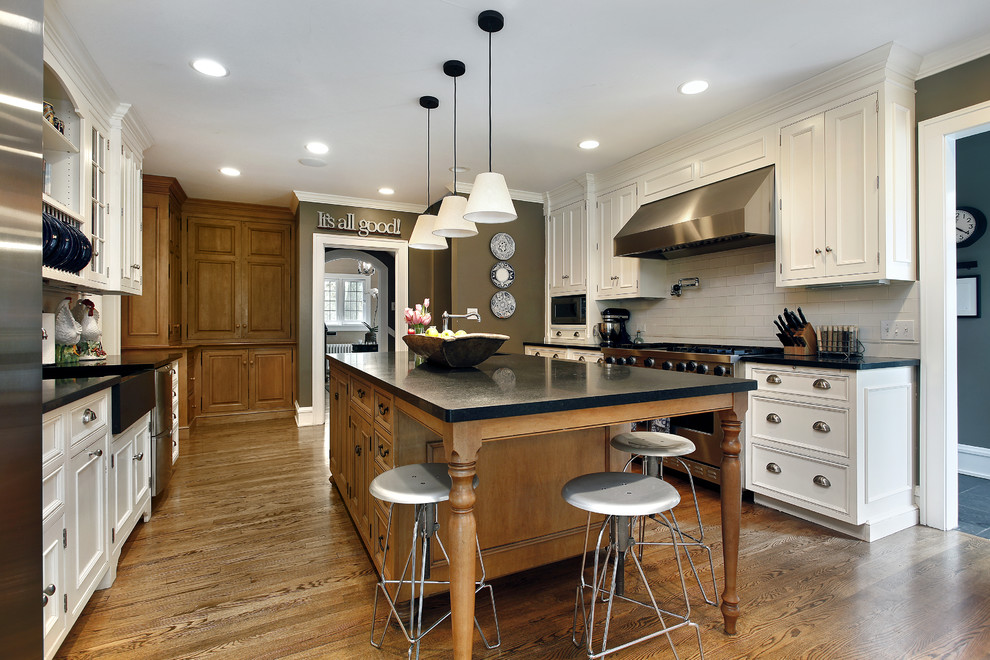 Design ideas for a large traditional galley eat-in kitchen in DC Metro with a farmhouse sink, shaker cabinets, white cabinets, quartz benchtops, white splashback, ceramic splashback, stainless steel appliances, light hardwood floors and with island.