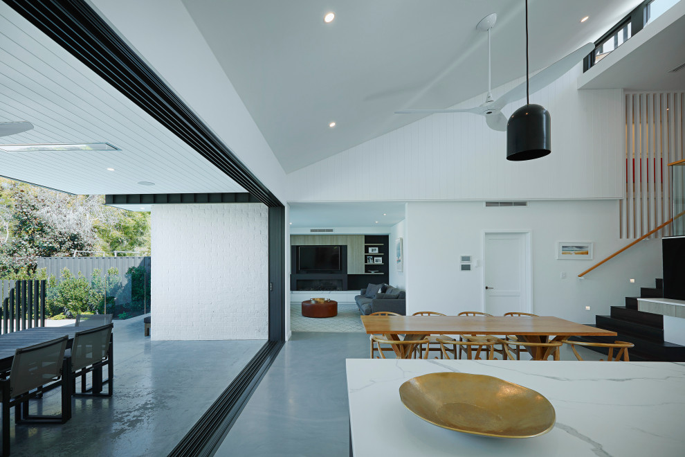 Idee per una sala da pranzo aperta verso la cucina minimalista di medie dimensioni con pareti bianche, pavimento in cemento, pavimento grigio, soffitto a volta, pannellatura e nessun camino