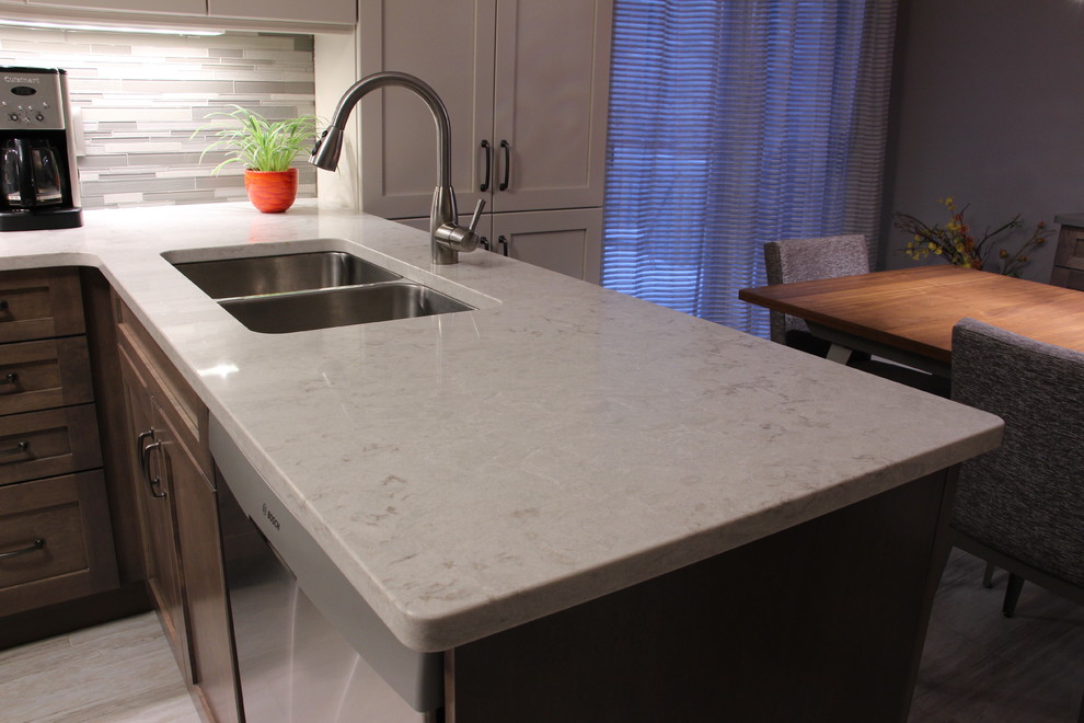 Inspiration for a transitional u-shaped ceramic tile and beige floor eat-in kitchen remodel in Toronto with a double-bowl sink, shaker cabinets, gray cabinets, solid surface countertops, gray backsplash, glass sheet backsplash, stainless steel appliances and no island