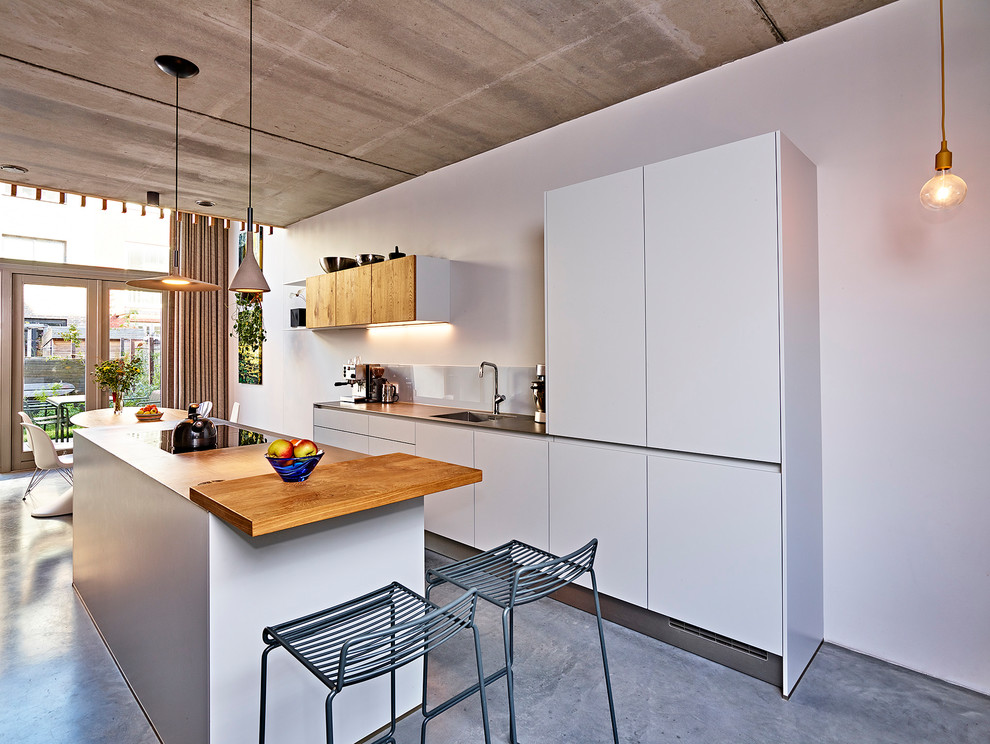 Inspiration for a mid-sized contemporary galley eat-in kitchen in Amsterdam with an integrated sink, flat-panel cabinets, grey cabinets, stainless steel benchtops, white splashback, glass sheet splashback, stainless steel appliances, concrete floors, with island and grey floor.