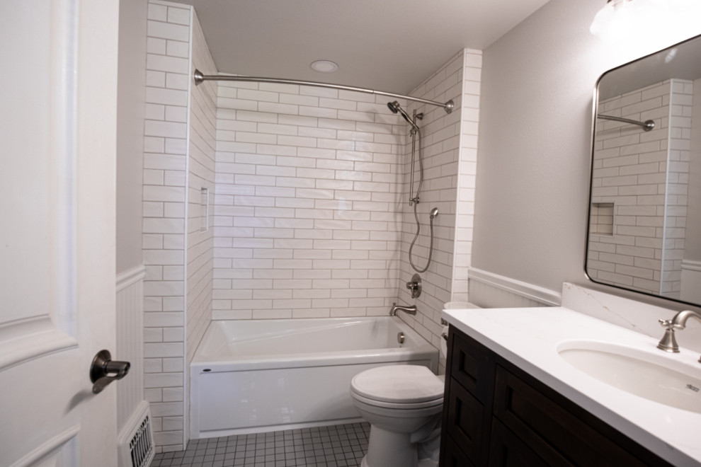 Bild på ett litet lantligt vit vitt en-suite badrum, med skåp i shakerstil, bruna skåp, ett badkar i en alkov, en dusch/badkar-kombination, en toalettstol med hel cisternkåpa, vit kakel, keramikplattor, grå väggar, klinkergolv i keramik, ett undermonterad handfat, bänkskiva i kvarts, grått golv och dusch med duschdraperi