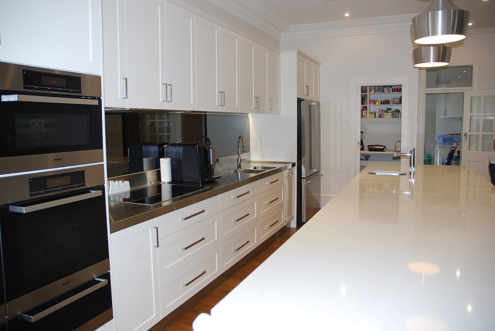 Inspiration for a large contemporary single-wall kitchen pantry in Sydney with a double-bowl sink, shaker cabinets, white cabinets, quartz benchtops, grey splashback, glass sheet splashback, stainless steel appliances, medium hardwood floors and with island.