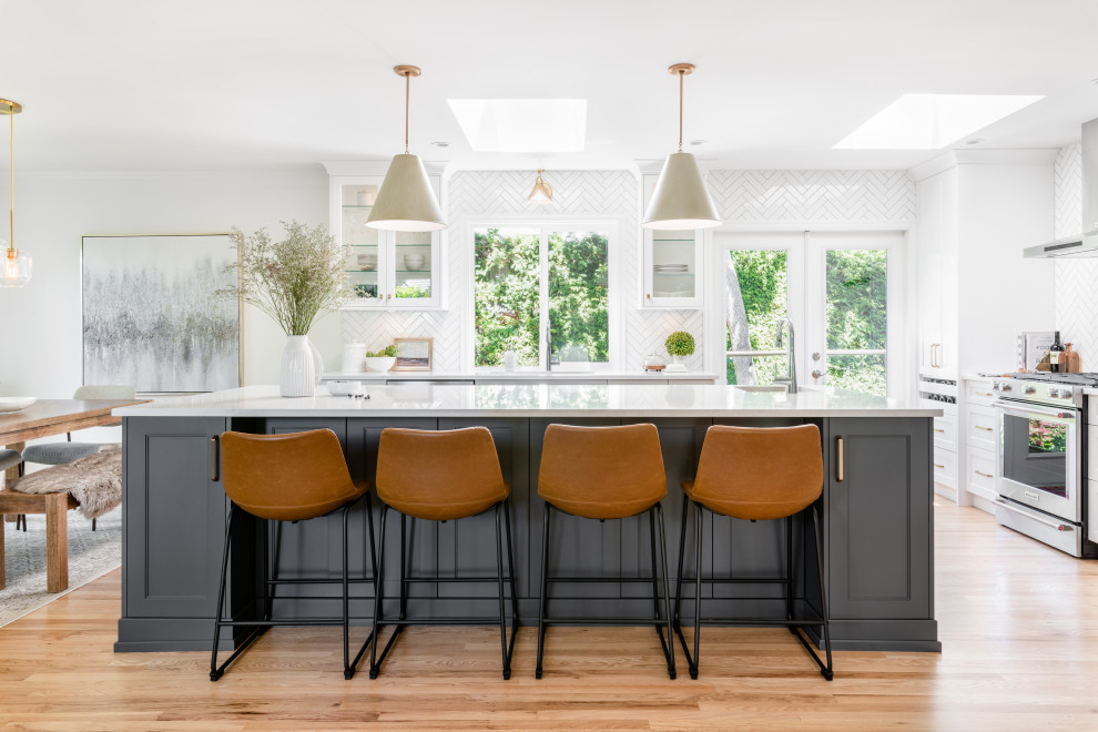 Inspiration for a large transitional l-shaped open plan kitchen in Vancouver with an undermount sink, recessed-panel cabinets, white cabinets, quartz benchtops, white splashback, ceramic splashback, stainless steel appliances, light hardwood floors, with island, beige floor and white benchtop.