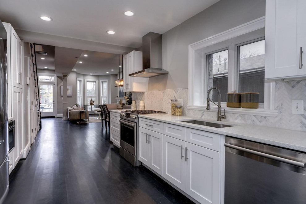 This is an example of a large transitional single-wall wet bar in DC Metro with an undermount sink, shaker cabinets, white cabinets, quartz benchtops, white splashback, porcelain splashback, dark hardwood floors, black floor and white benchtop.