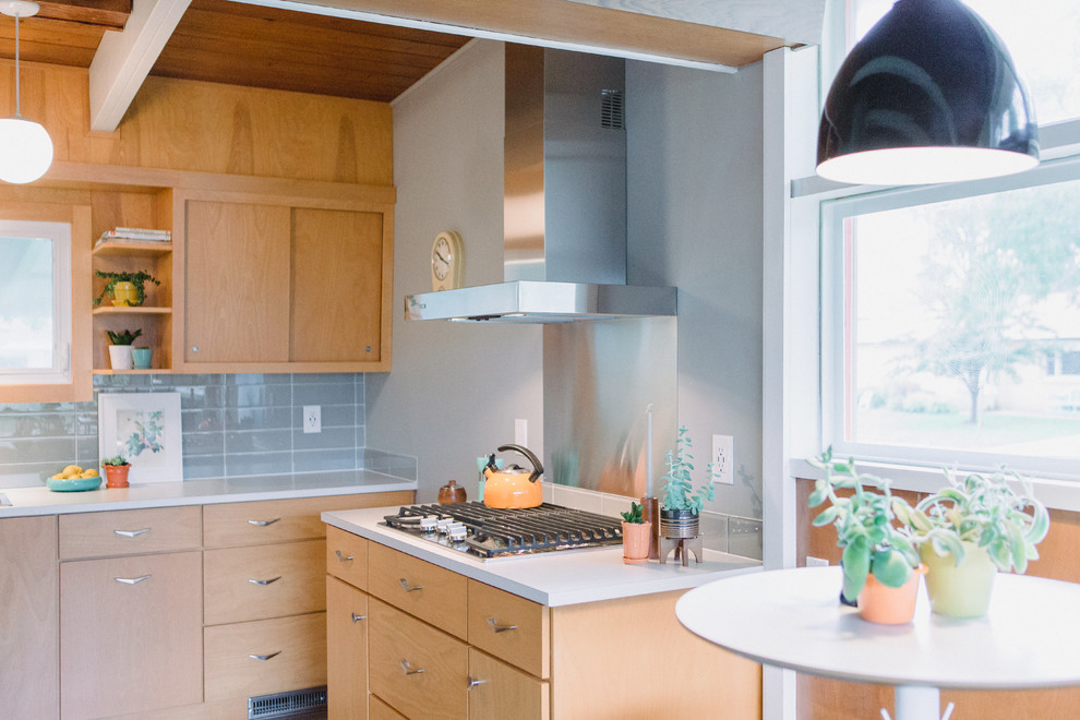 This is an example of a small midcentury galley separate kitchen in Grand Rapids with a drop-in sink, flat-panel cabinets, light wood cabinets, laminate benchtops, grey splashback, glass tile splashback, stainless steel appliances, medium hardwood floors, no island, grey floor and beige benchtop.