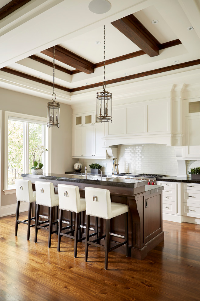Example of a large transitional l-shaped medium tone wood floor open concept kitchen design in Toronto with recessed-panel cabinets, white cabinets, granite countertops, white backsplash, subway tile backsplash, stainless steel appliances and an island