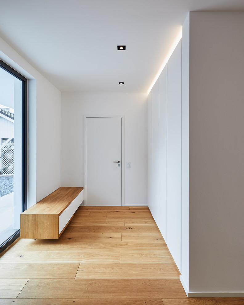 Photo of a mid-sized modern hallway in Dusseldorf with white walls, medium hardwood floors and brown floor.