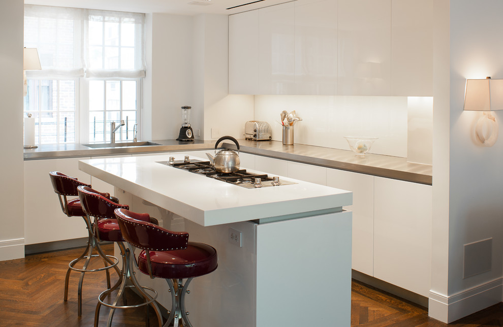 Photo of a large contemporary l-shaped eat-in kitchen in New York with an undermount sink, flat-panel cabinets, white cabinets, stainless steel appliances, medium hardwood floors and with island.