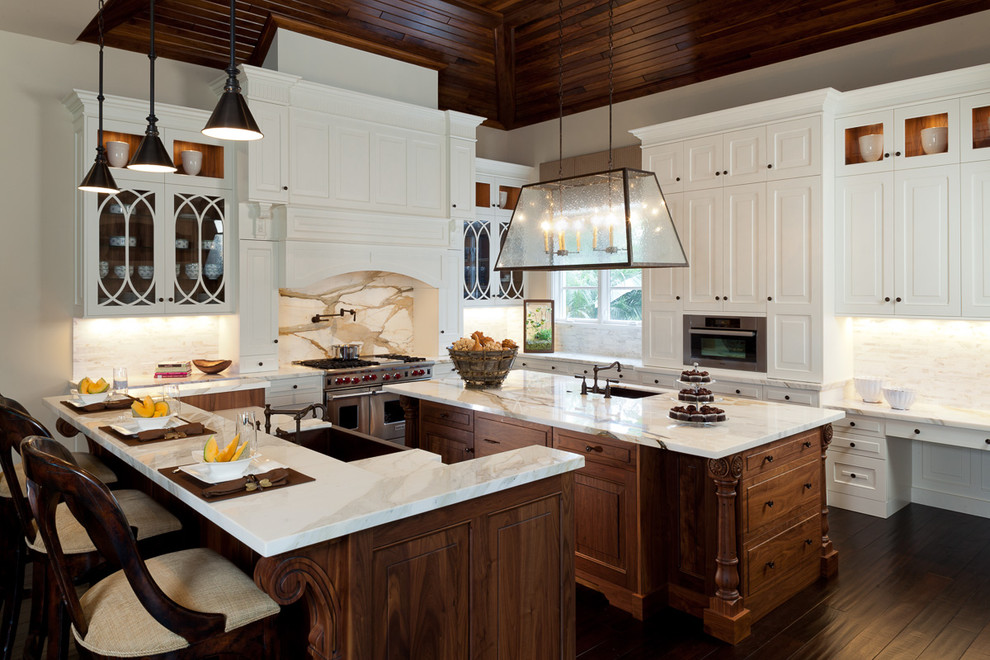 Photo of a large traditional u-shaped eat-in kitchen in Miami with a farmhouse sink, raised-panel cabinets, white cabinets, white splashback, stainless steel appliances, marble benchtops, marble splashback, dark hardwood floors, multiple islands and brown floor.